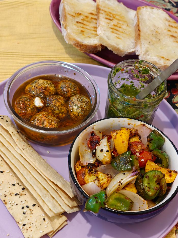 Close-up of an Indian vegetarian platter featuring labneh balls, grilled vegetables, and herbs.